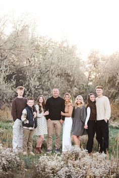 a family posing for a photo in front of some trees and bushes with their arms around each other