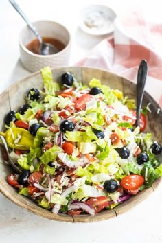 a salad with olives, lettuce, tomatoes and blueberries in a bowl