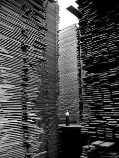 a black and white photo of a person standing in front of stacks of wooden boxes