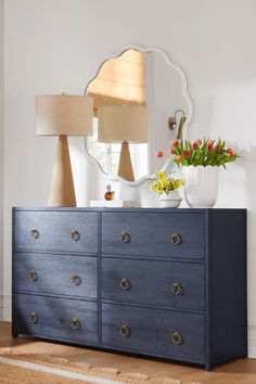 a blue dresser with flowers on top and a mirror above it in a white room