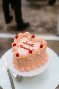 a heart shaped cake with cherries on top sitting on a table next to a knife and fork