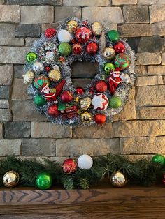 a christmas wreath is hanging on a stone wall next to ornaments and greenery in front of a fireplace