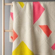 a white blanket with pink, yellow and orange designs on it hanging from a wooden ladder