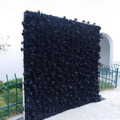 a large black piece of art sitting on top of a cement ground next to a fence