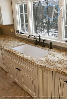 a kitchen with granite counter tops and white cabinets in front of two windows that look out onto the woods