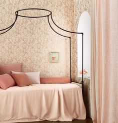 a bed with pink sheets and pillows in a room next to a curtained window