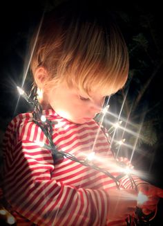 a young child holding a string of lights in her hands and looking down at the ground