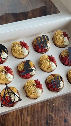 twelve decorated cupcakes in a white box on a wooden table, with harry potter symbols