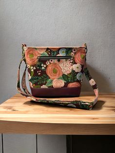 a purse sitting on top of a wooden table next to a gray wall with flowers