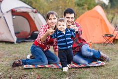 a man, woman and child sitting on a blanket in front of a camp site