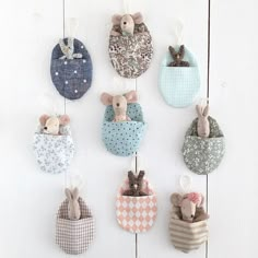 several small stuffed animals hanging from hooks on a white wall with wooden boards behind them