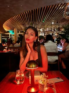 a beautiful woman sitting at a table in front of a wine glass and candle holder