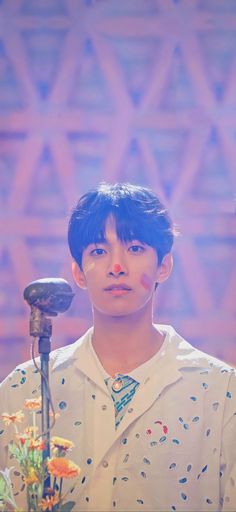 a young man standing in front of a microphone with flowers around his neck and face