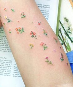 a woman's arm with flowers on it and an open book in the background