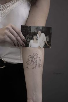 a woman with a small tattoo on her arm holding up a photo and looking at the camera