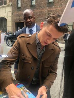 a man in a trench coat looking at something on a table with other people around him