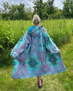 a woman is walking in the grass wearing a blue and green dress with feathers on it