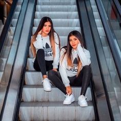 two young women sitting on an escalator wearing adidas sweatshirts and leggings