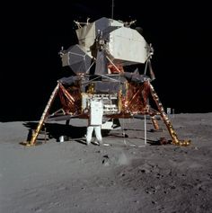 an astronaut standing on the moon next to a satellite device with two astronauts in it