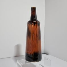 a brown and black vase sitting on top of a white shelf