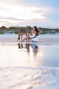 a woman kneeling down with her dog on the beach in front of water and sand