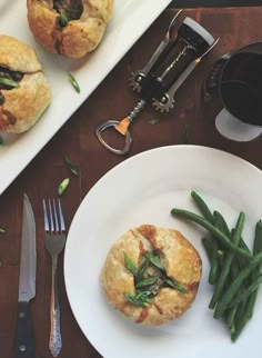 two white plates topped with pastries and green beans next to silverware on a wooden table