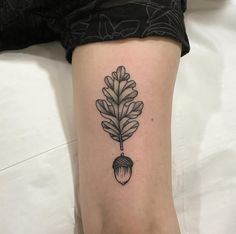 a black and white image of an acorn tattoo on the leg