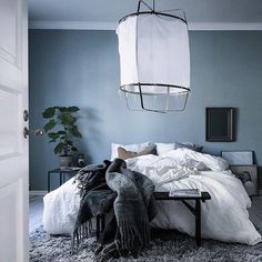 a bed with white sheets and pillows in a bedroom next to a plant hanging from the ceiling