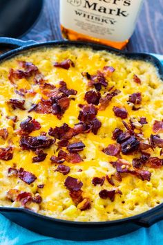 a casserole dish with bacon and cheese in it next to a bottle of beer