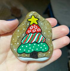 a hand holding a rock with a christmas tree painted on it