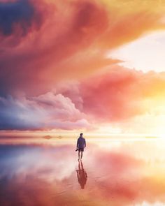 a man standing on top of a sandy beach under a cloudy blue and orange sky