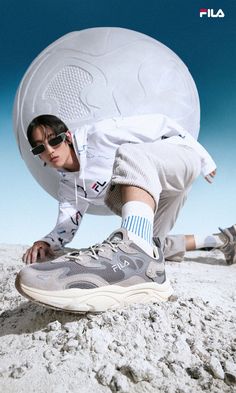 a woman in sunglasses and sneakers leaning against a large object on the ground with her legs spread out