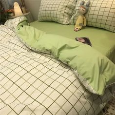 a bed with green comforter and pillows on top of it next to a stuffed animal