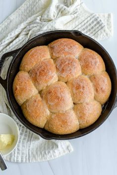 a cast iron skillet filled with bread on top of a white table next to a bowl of butter