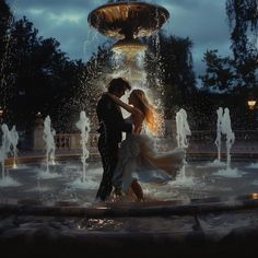 a bride and groom dancing in front of a fountain at night with the lights on