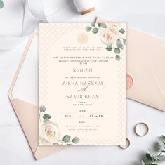 an elegant wedding card with roses and greenery on it, next to a pair of scissors