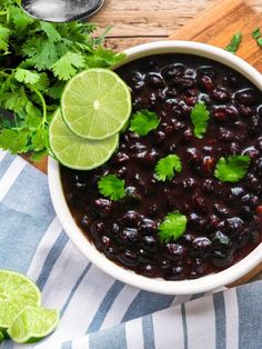 a white bowl filled with black beans and garnished with cilantro next to limes