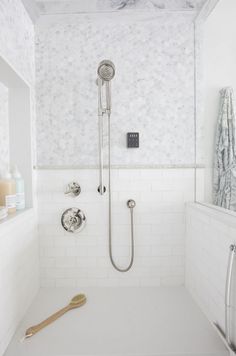 a white tiled bathroom with a shower head and hand held shower faucet in the corner