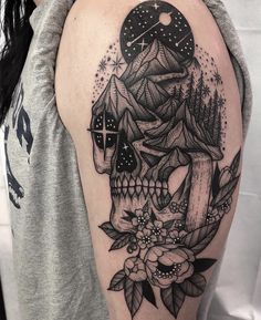 a black and white tattoo with a skull on the left side of the arm, surrounded by flowers