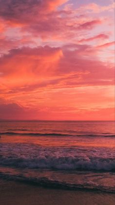 a person walking on the beach with a surfboard under a pink sky at sunset