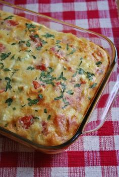 a casserole dish with tomatoes, cheese and herbs in it on a red checkered tablecloth