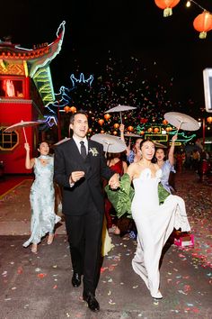 a bride and groom walk down the aisle with umbrellas in hand as confetti falls around them