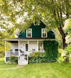 a green and white house surrounded by lush greenery on a sunny day in the country