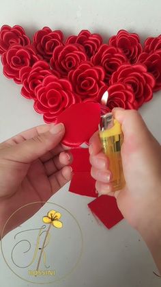 a person holding a small bottle in front of a heart shaped paper sculpture with roses on it