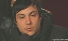 a young man with black hair and piercings on his ear is talking into a microphone