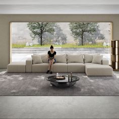 a woman sitting on top of a couch in front of a large window next to a coffee table