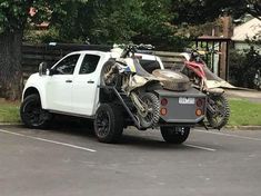 a white truck with an atv on the back is parked in a parking lot next to a tree