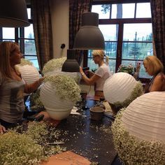 several women sitting around a table with paper lanterns and flowers on it in front of large windows