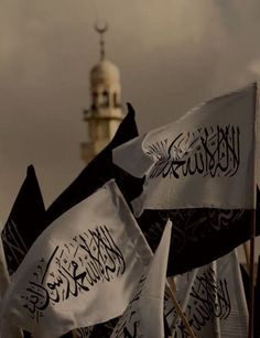 several black and white flags with arabic writing on them in front of a building that has a clock tower