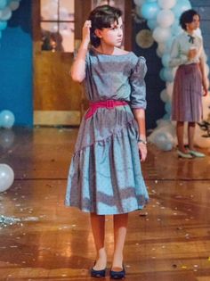 a woman in a dress standing on a wooden floor next to balloons and confetti